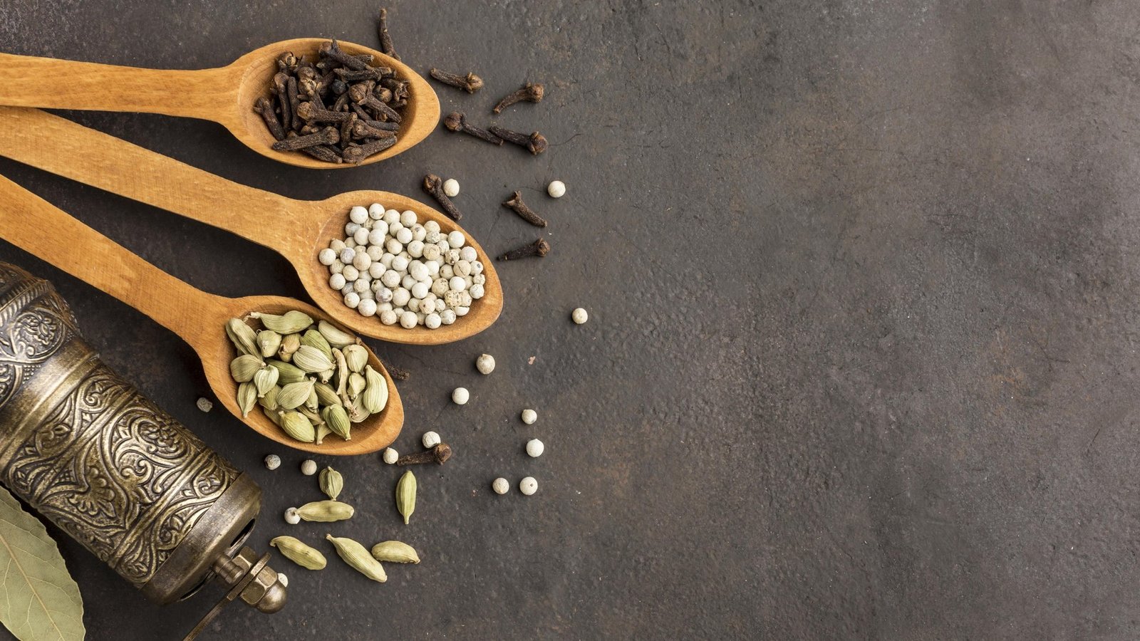 Cloves, white pepper and cardamom on wooden spoons